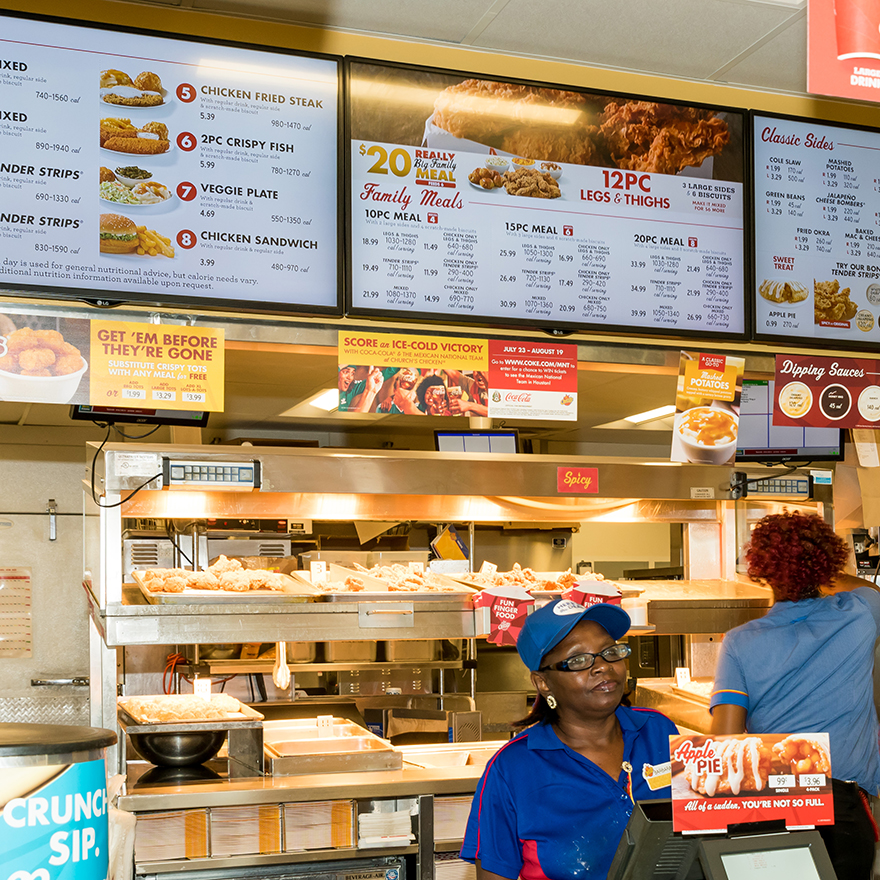 Two people standing in front of a Church's Chicken counter while placing an order with a cashier.