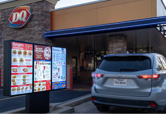 A car pulls past a Dairy Queen drive-thru board.