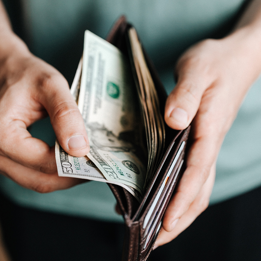 A close-up of two hands opening a trifold wallet with cash inside.