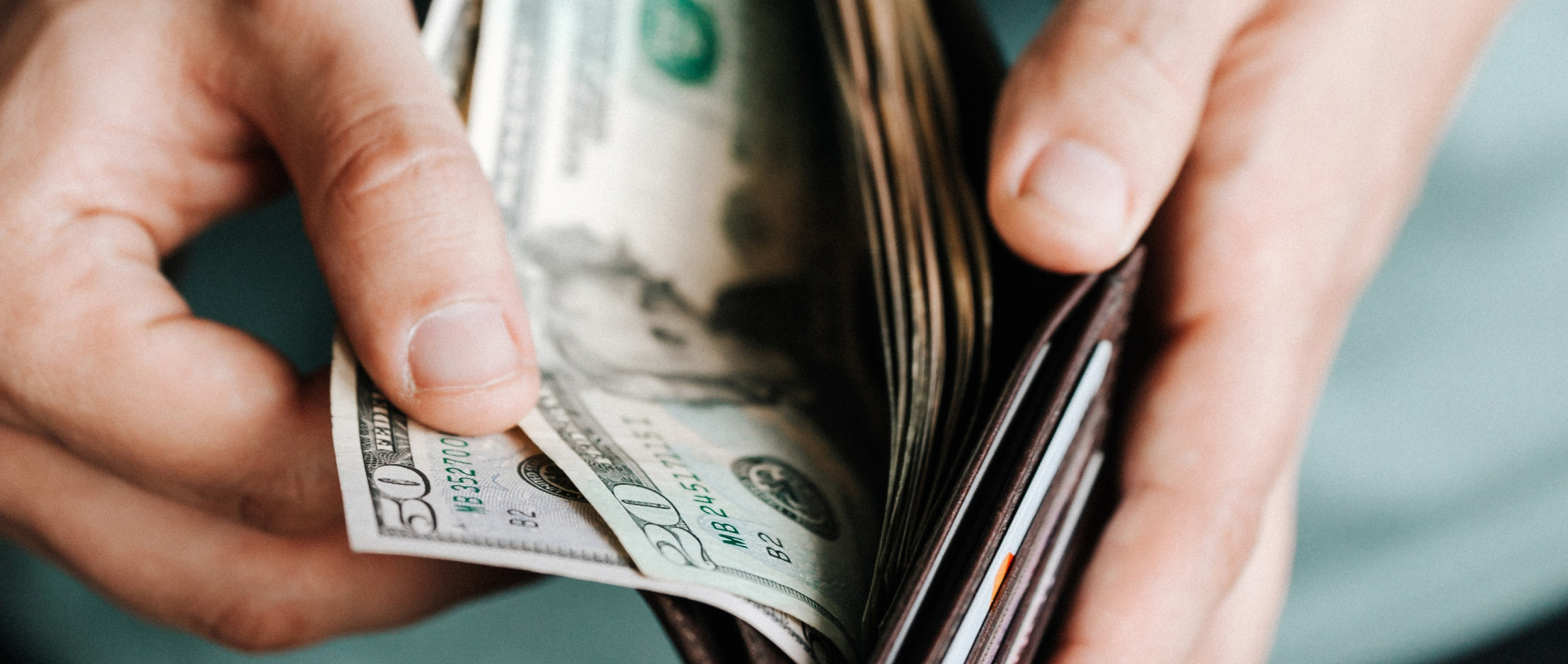 A close-up of two hands opening a trifold wallet with cash inside.